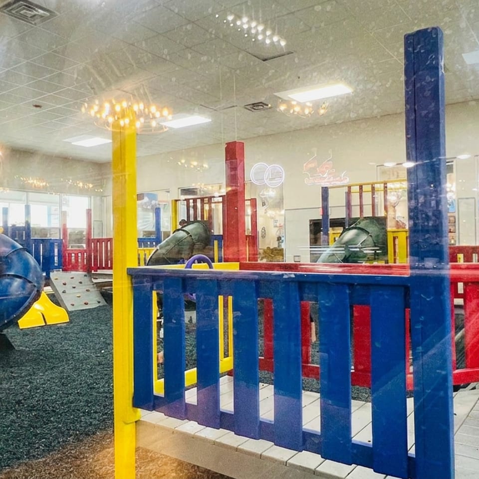 Colorful indoor restaurant play area with slides, climbing structures, ball pits, and bright red, blue, and yellow railings.